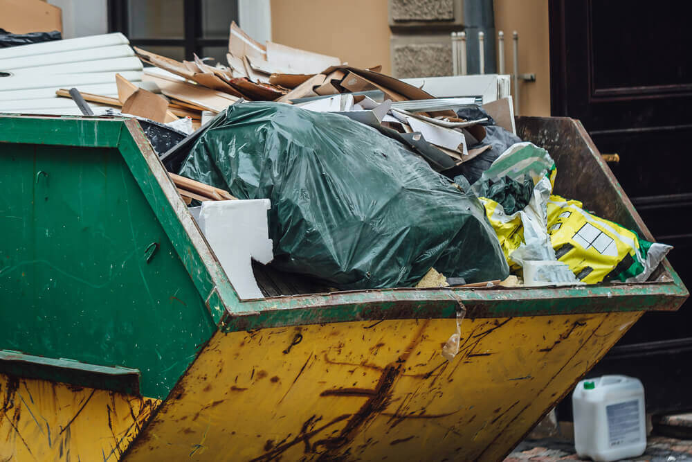 close up view of a yellow and green residential skip hire bin filled with household rubbish